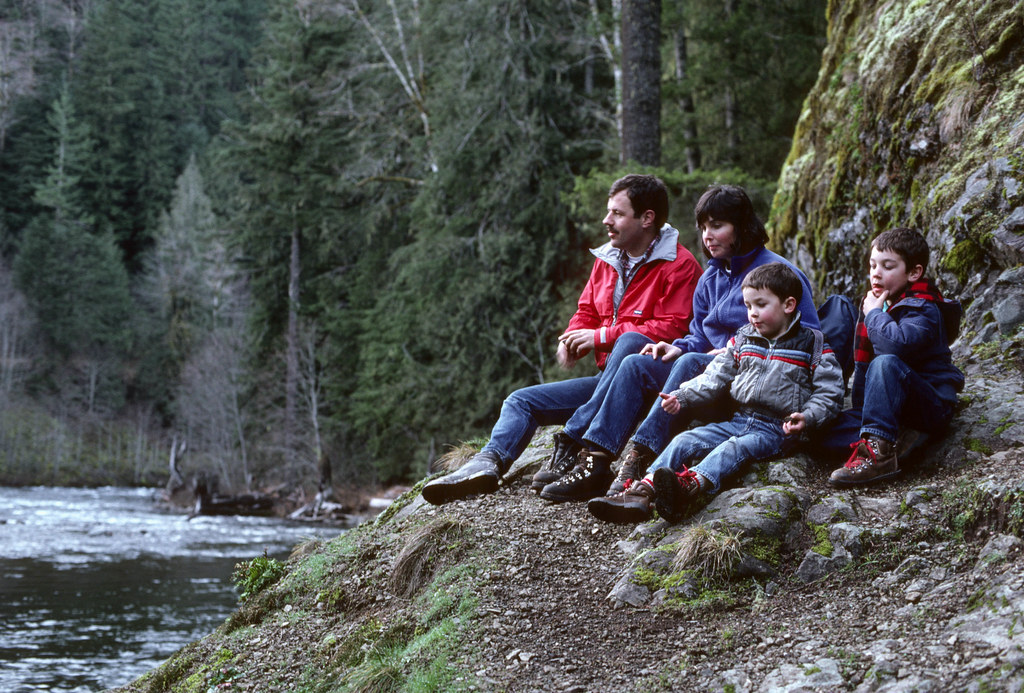 Family with two children resting beside a forest river during an outdoor walk